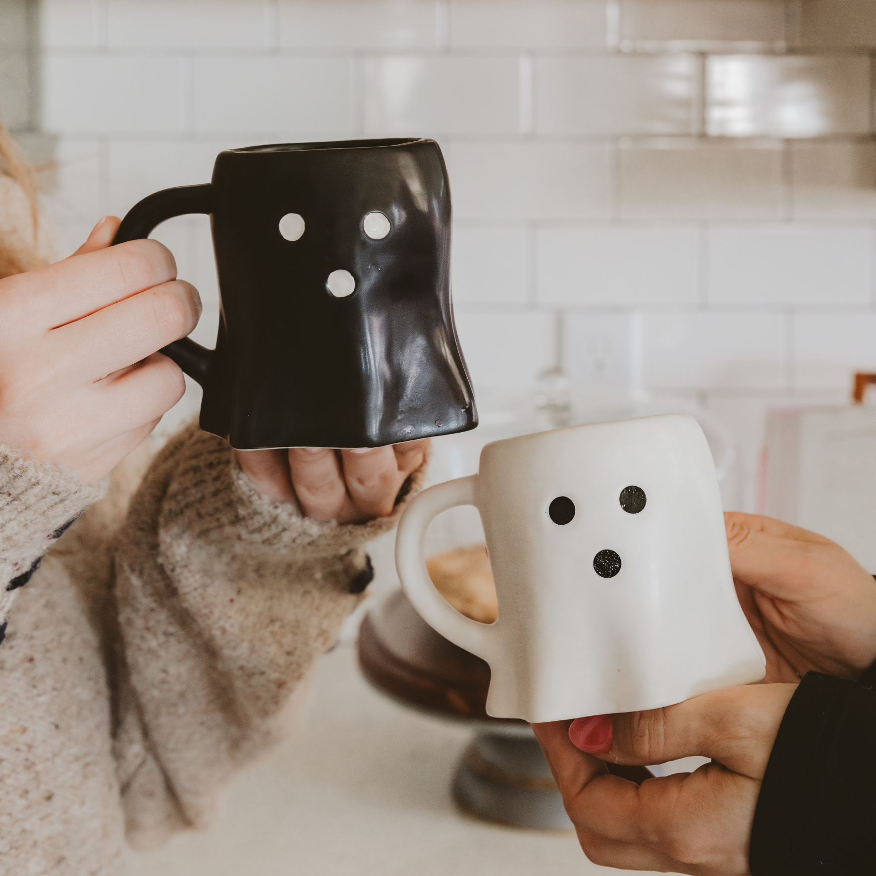 Two people holding black and white mugs with smiley face designs in a kitchen setting.