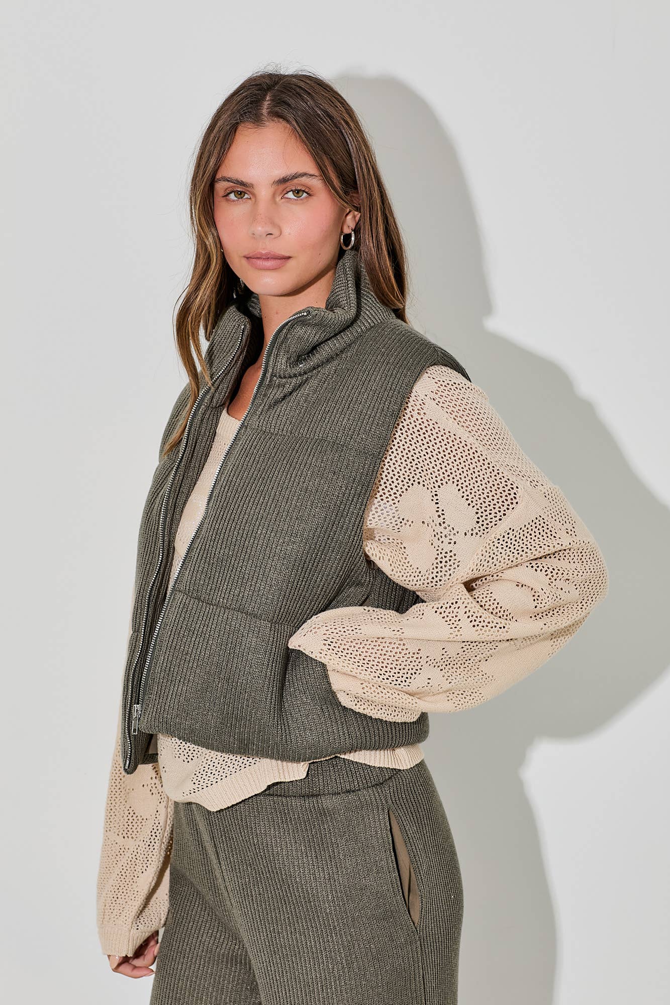 Woman wearing a green knit vest over a beige sweater with a plain background