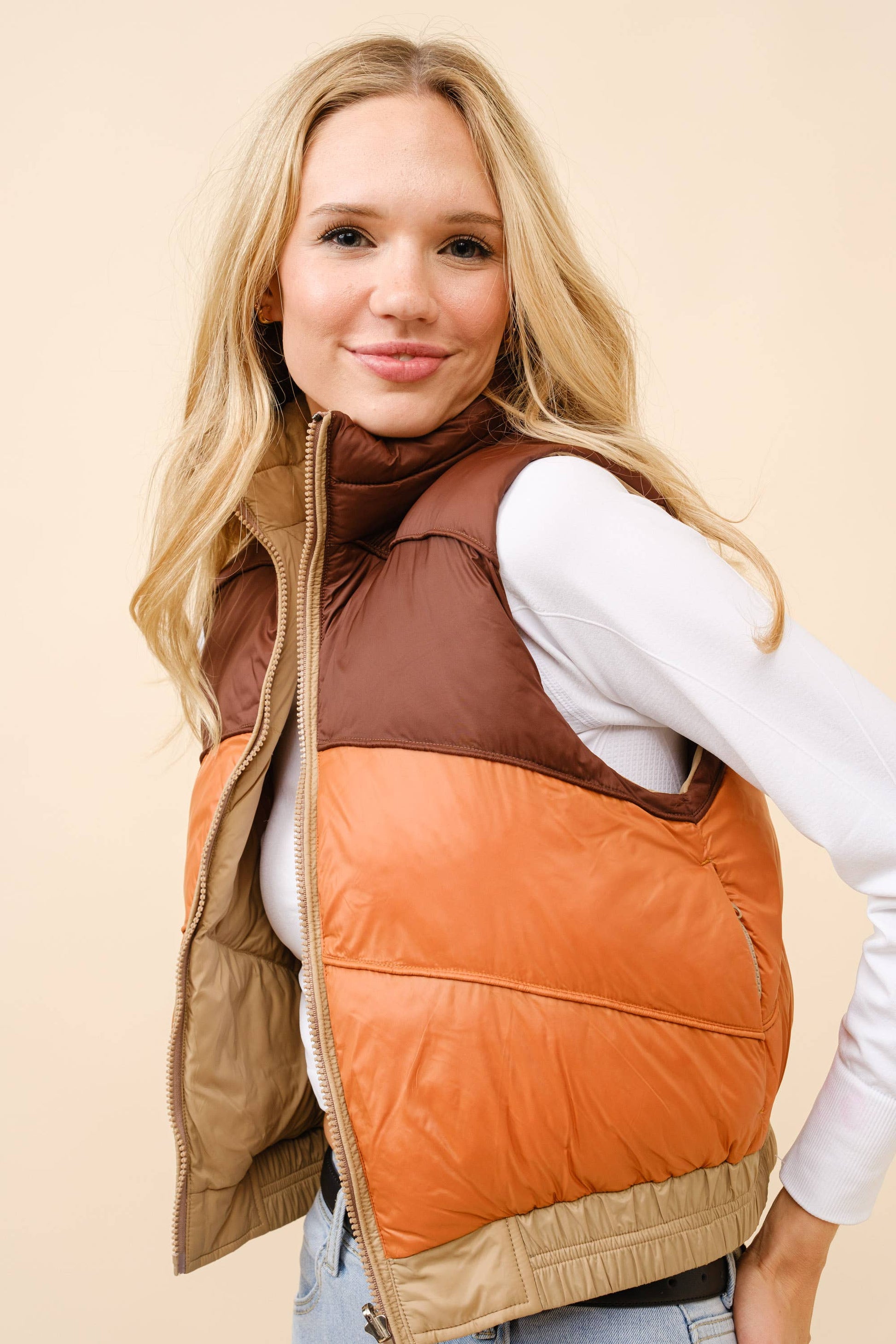 Woman wearing a brown and orange quilted vest on a beige background