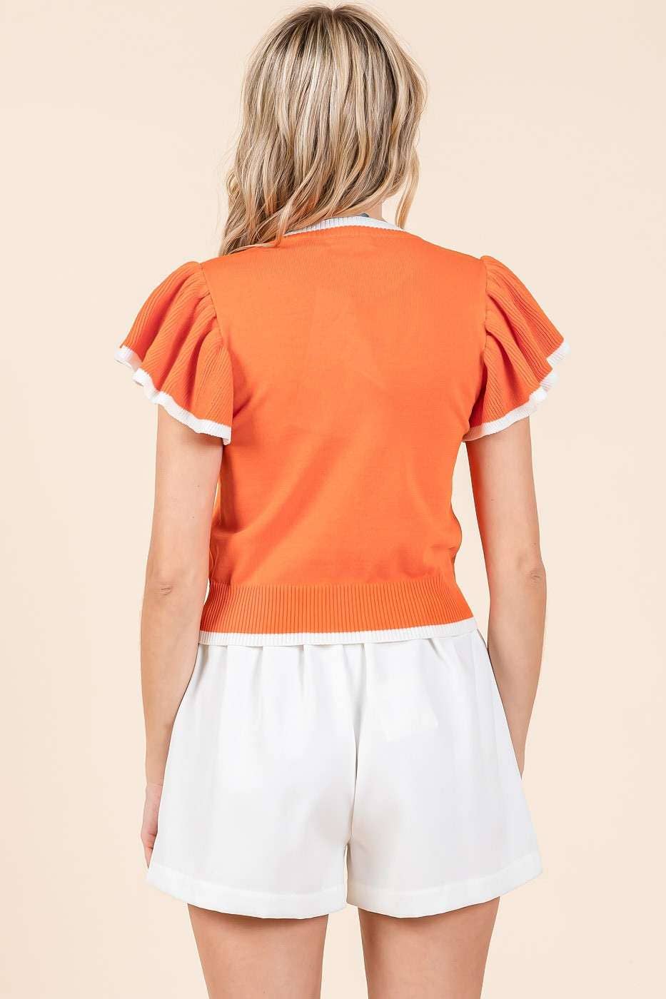 Person wearing an orange top with white trim and white shorts on a beige background