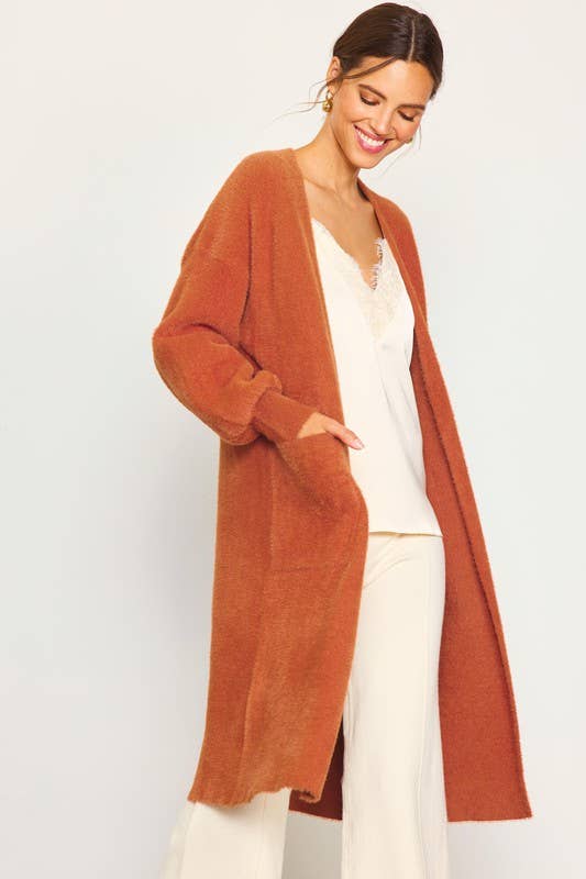 Woman wearing a long rust-colored cardigan over a white top and pants on a light gray background
