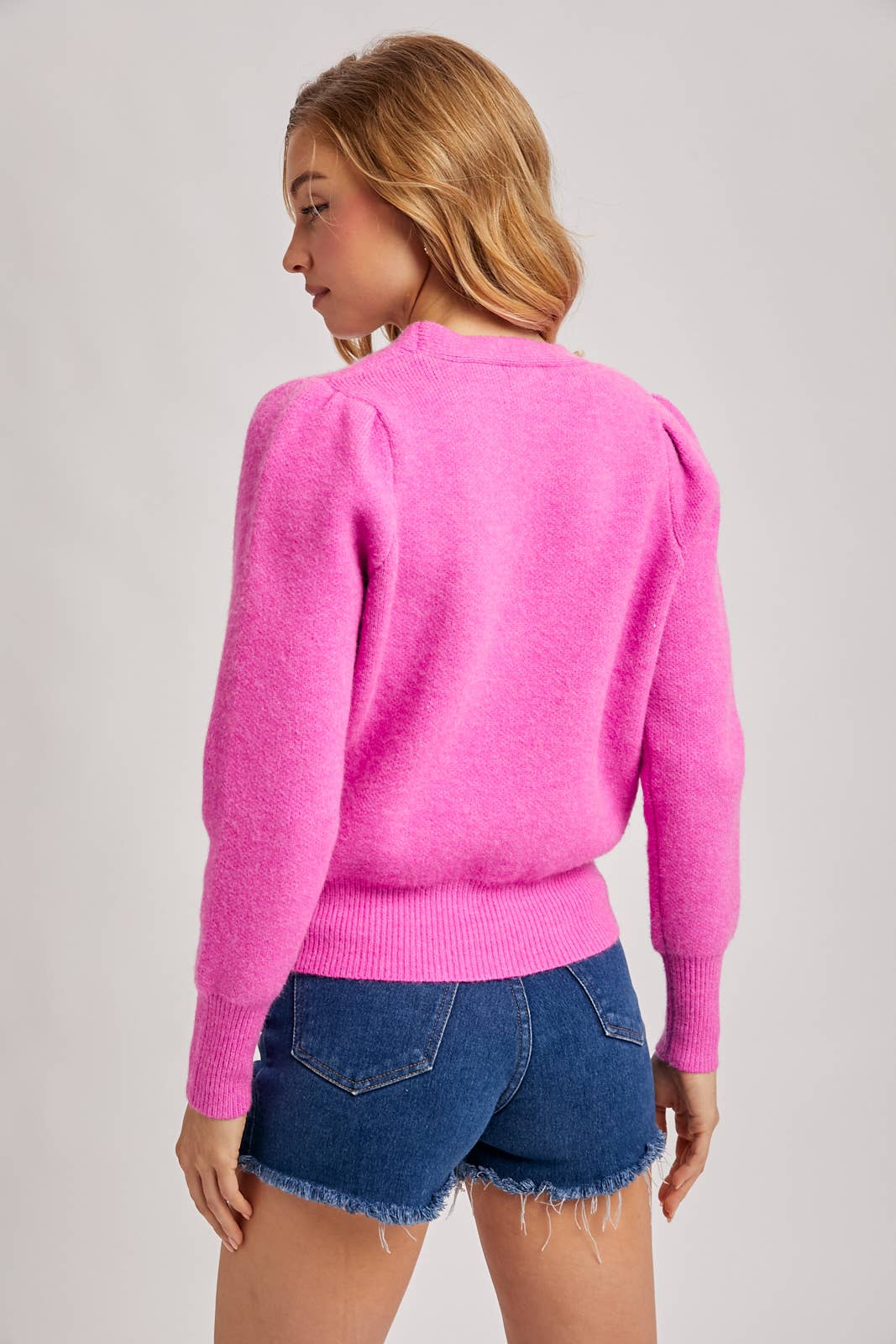 Person wearing a bright pink sweater and denim shorts on a plain background