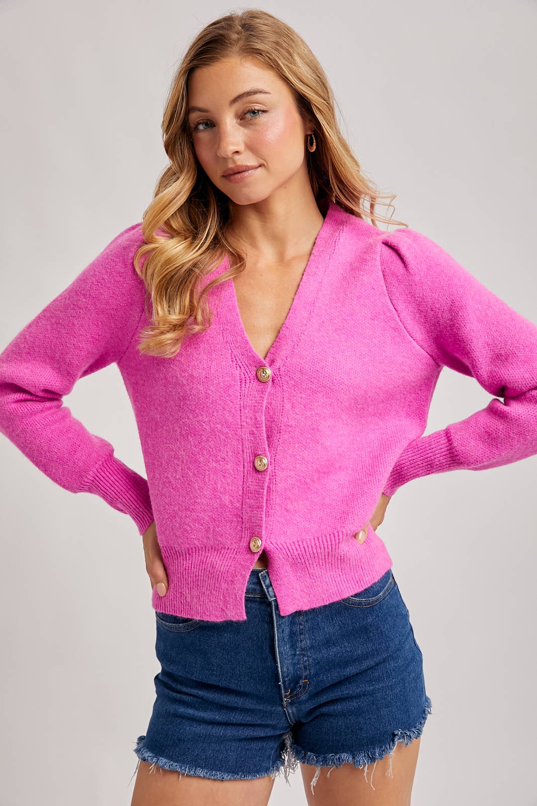 Woman wearing a pink cardigan and denim shorts on a plain background