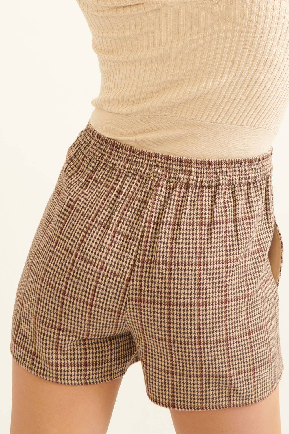 Plaid shorts worn with a beige top on a plain background