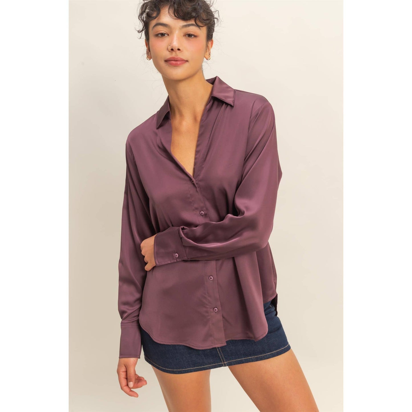 Woman wearing a mauve button-up shirt over a denim skirt on a beige background