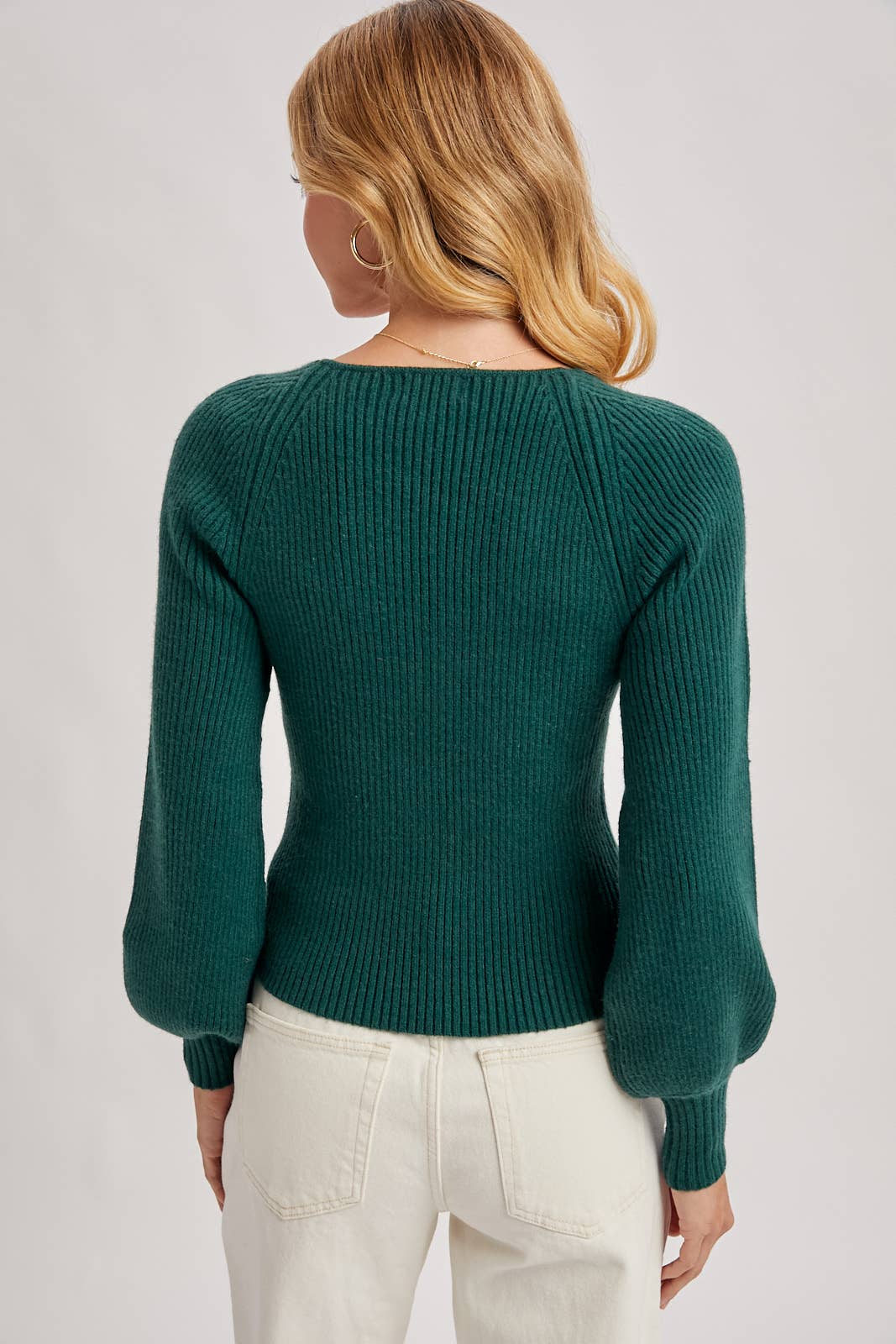Person wearing a green sweater and white pants on a light gray background
