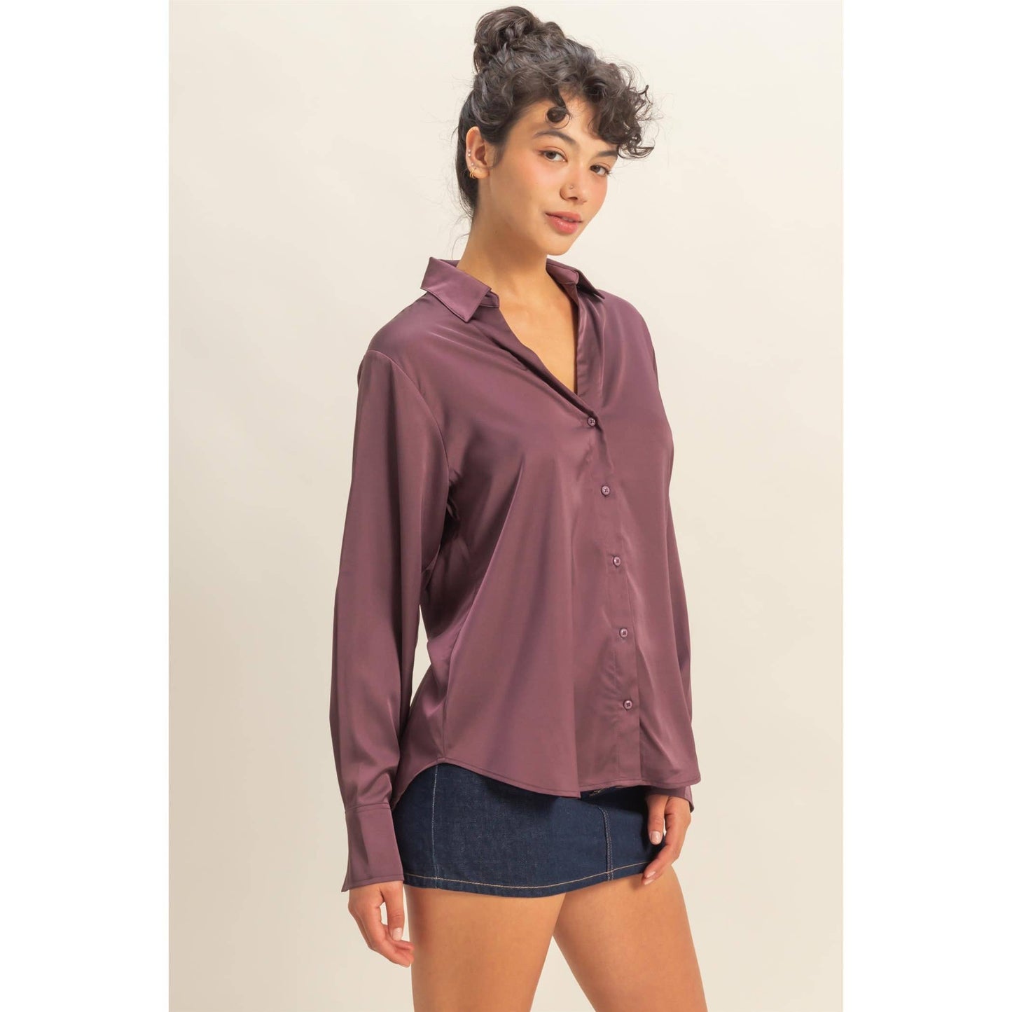 Woman wearing a mauve button-up shirt and denim shorts on a beige background