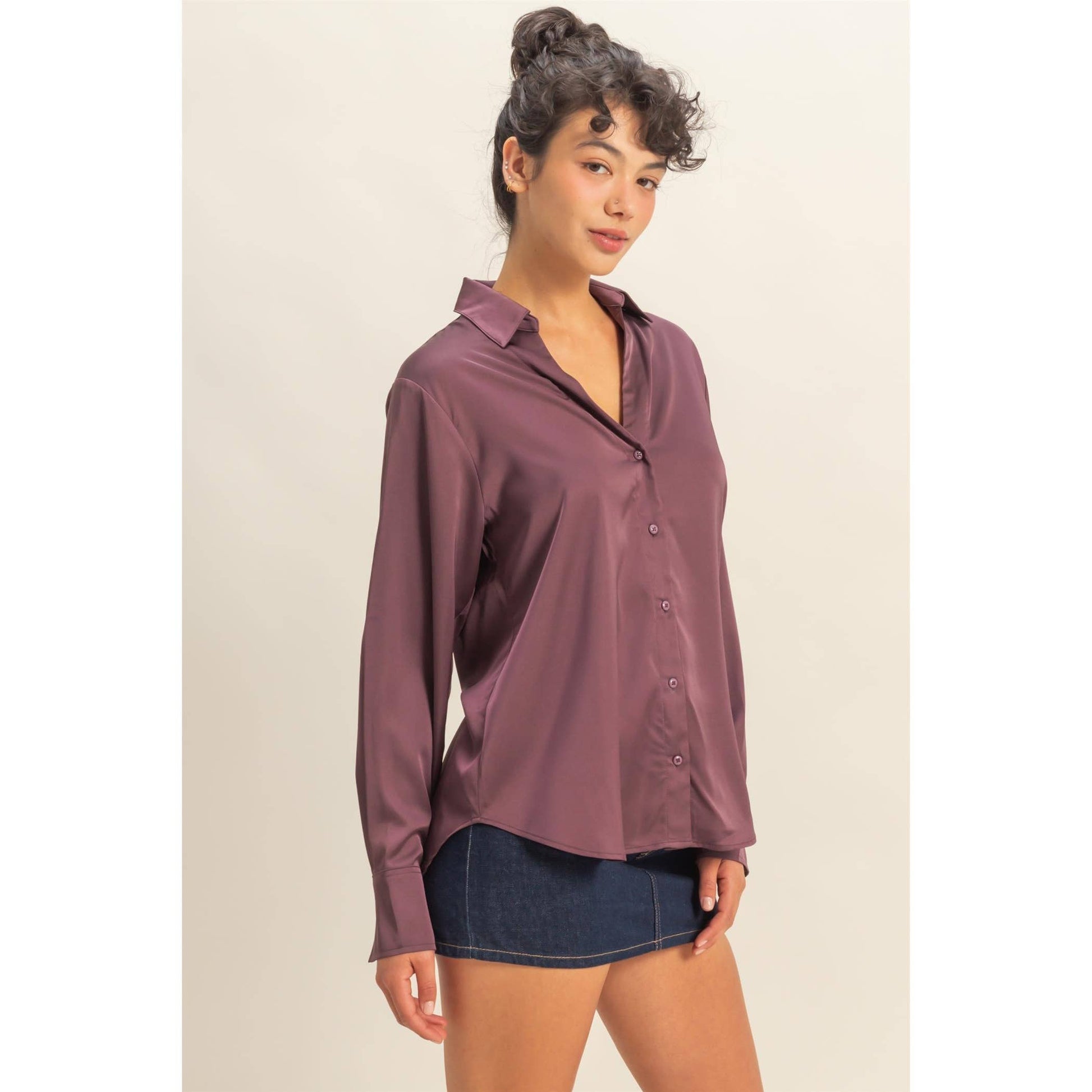 Woman wearing a mauve button-up shirt and denim shorts on a beige background