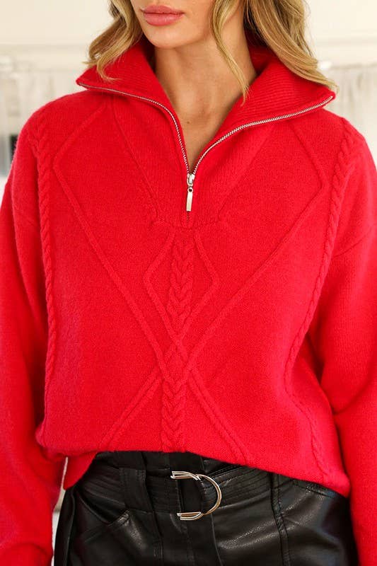 Red cable knit sweater worn by a person with a blurred background
