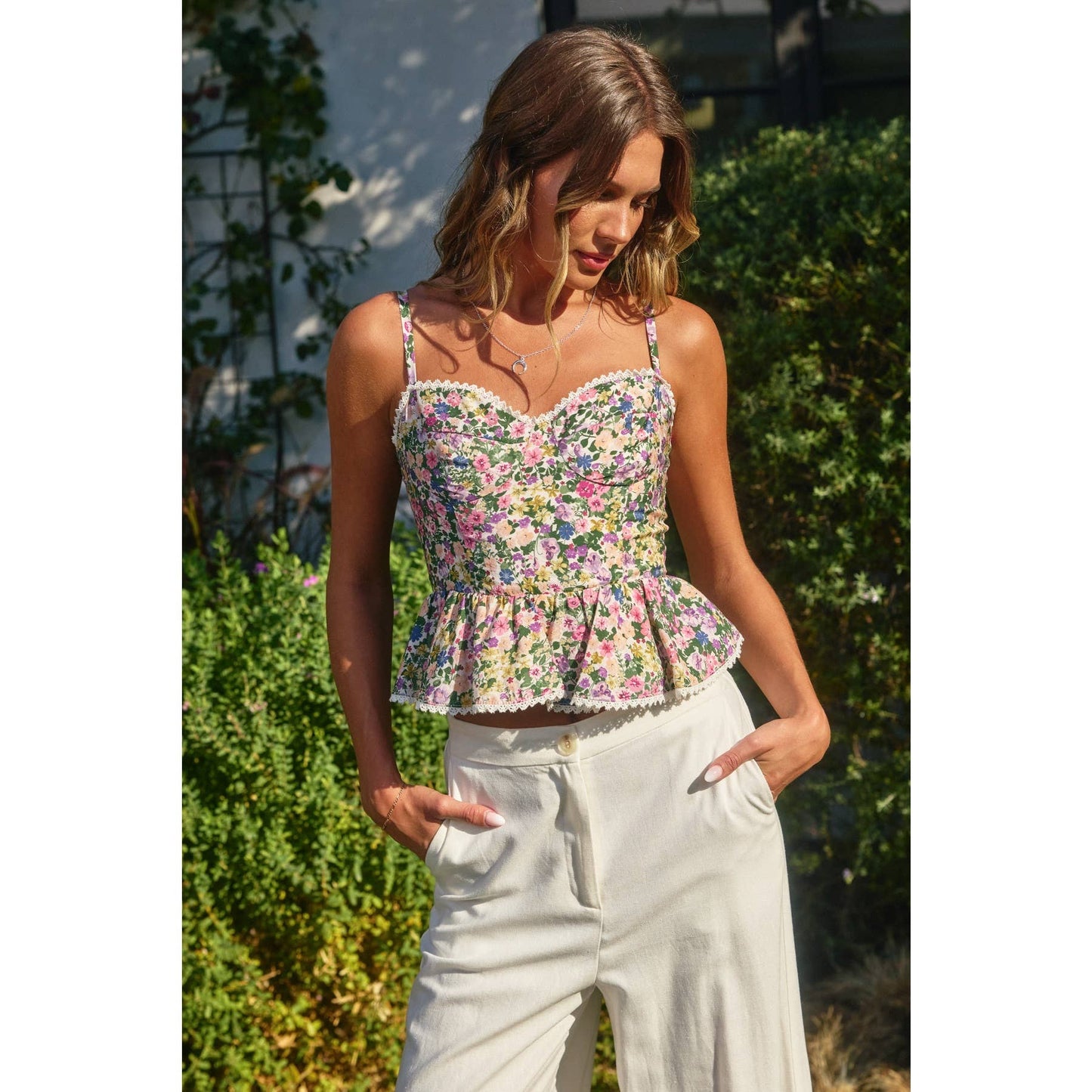 Woman wearing a floral peplum top and white pants outdoors.