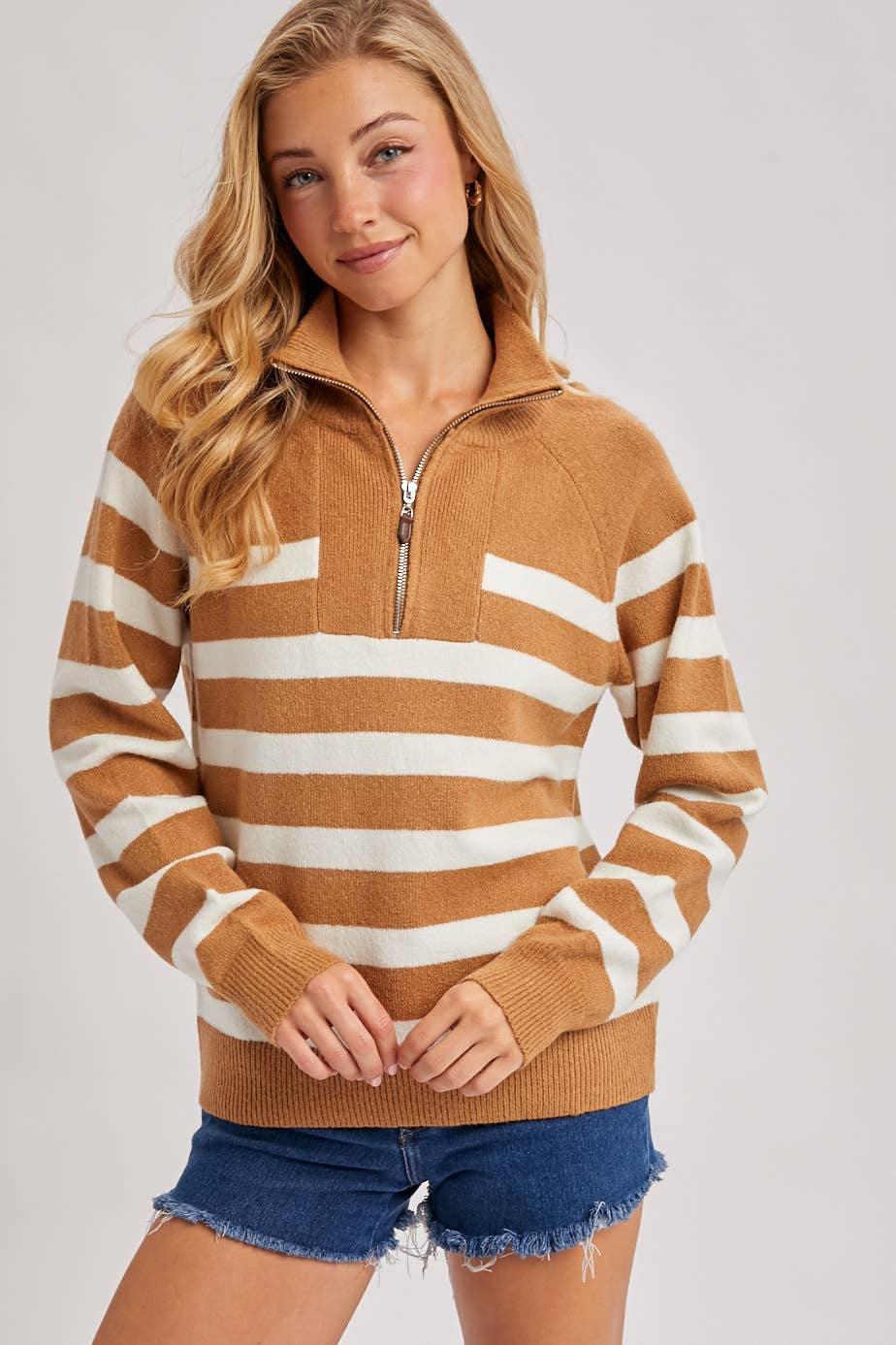 Woman wearing a brown and white striped sweater with a zipper on a plain background
