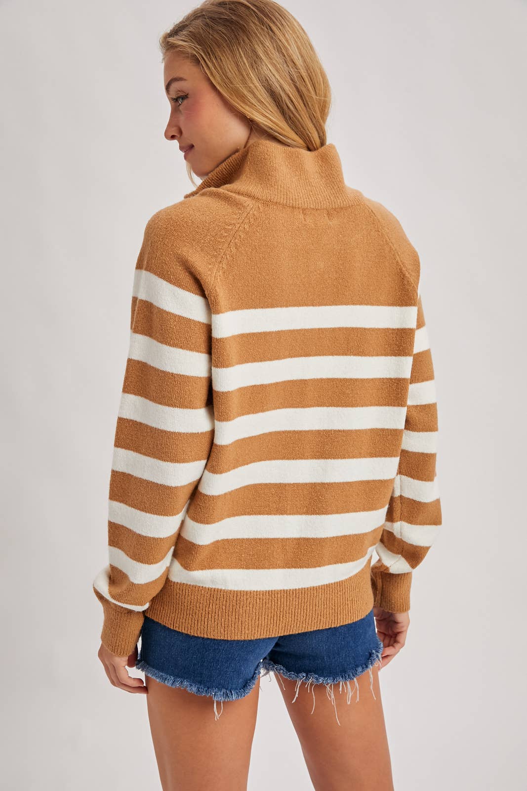 Woman wearing a brown and white striped sweater with denim shorts on a plain background