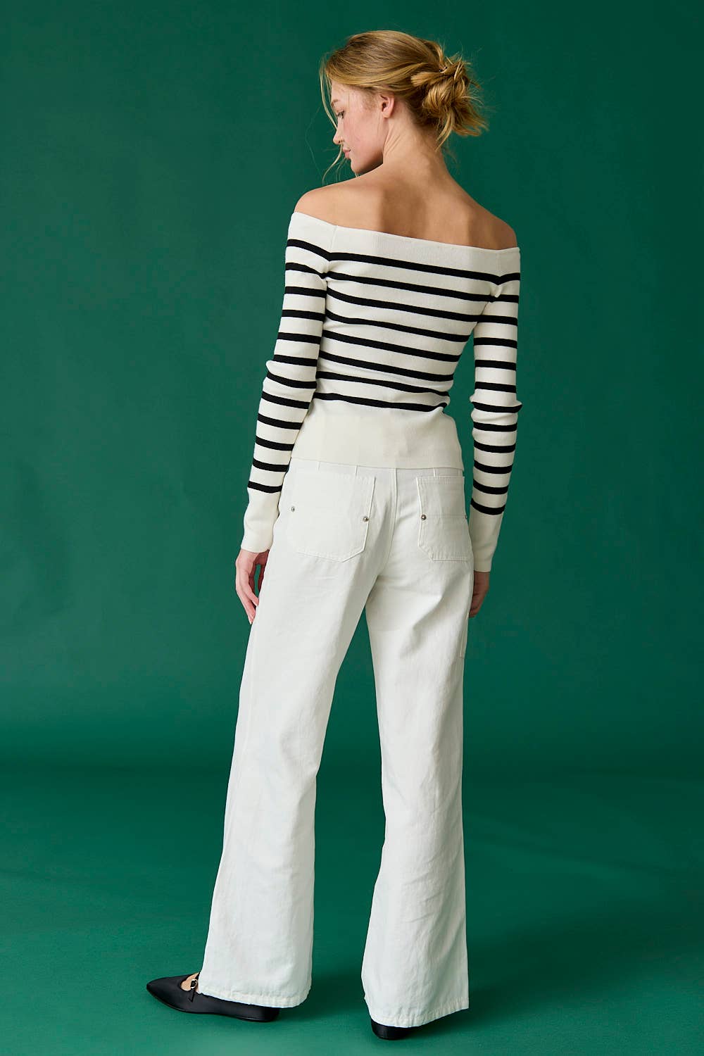 Woman wearing a black and white striped sweater and white pants against a green background