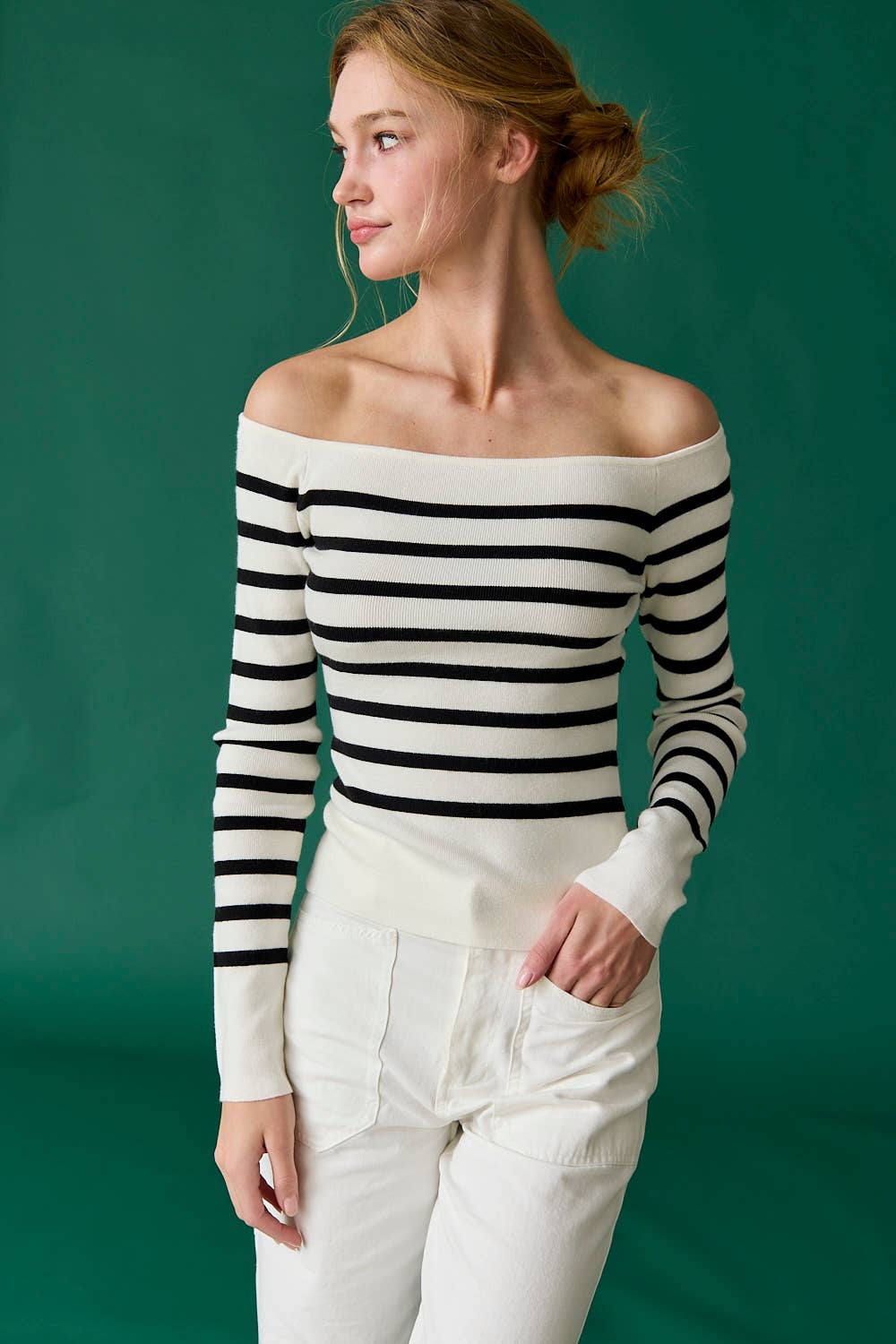 Woman wearing a black and white striped off-shoulder top with white pants against a green background