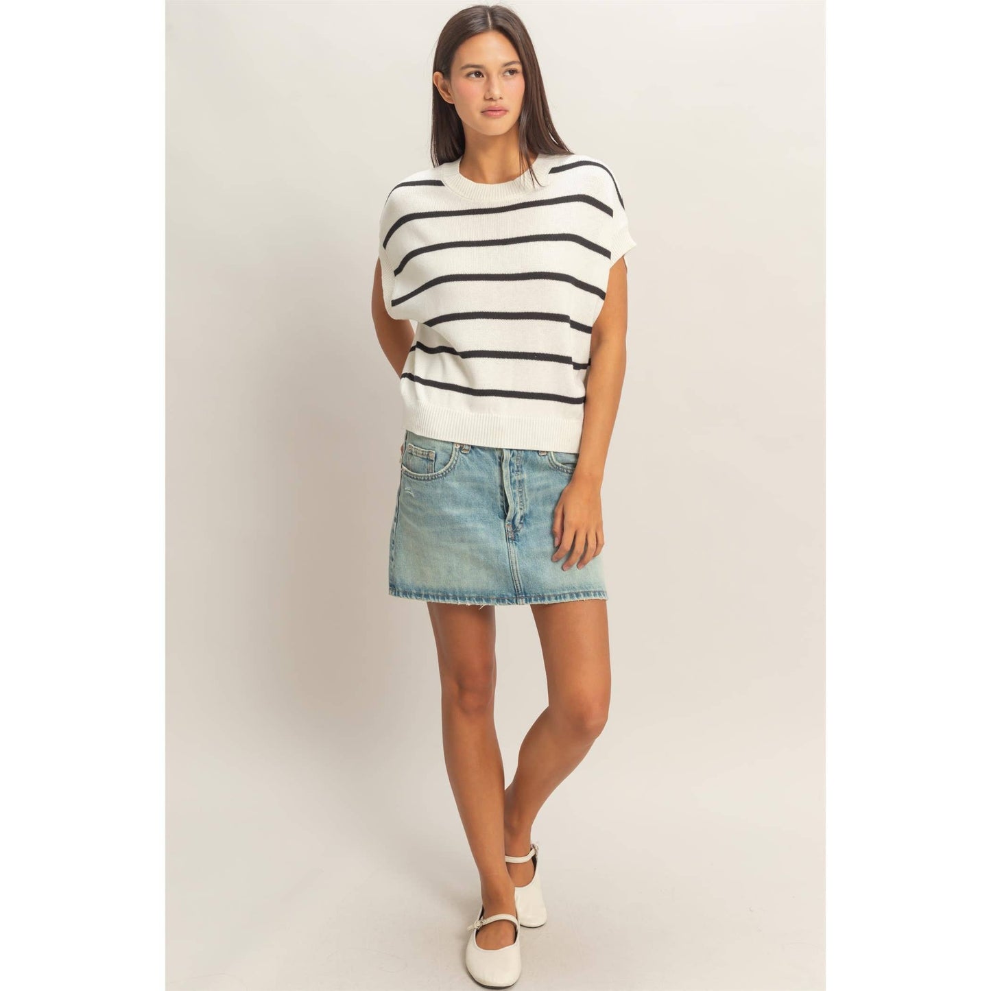 Woman wearing a black and white striped sleeveless top and denim skirt on a plain background