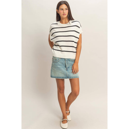 Woman wearing a black and white striped sleeveless top and denim skirt on a plain background