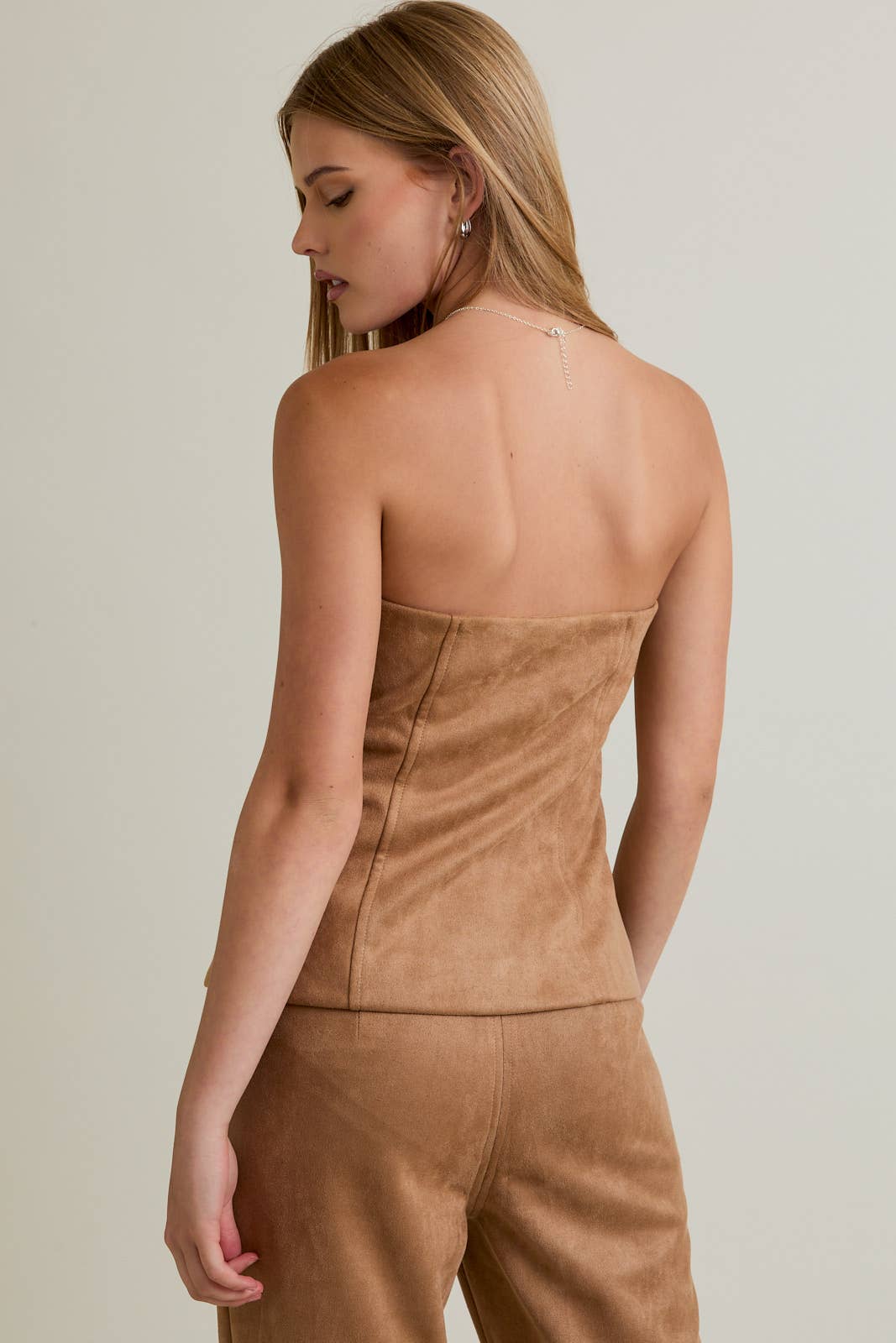 Woman wearing a brown strapless top and pants against a plain background