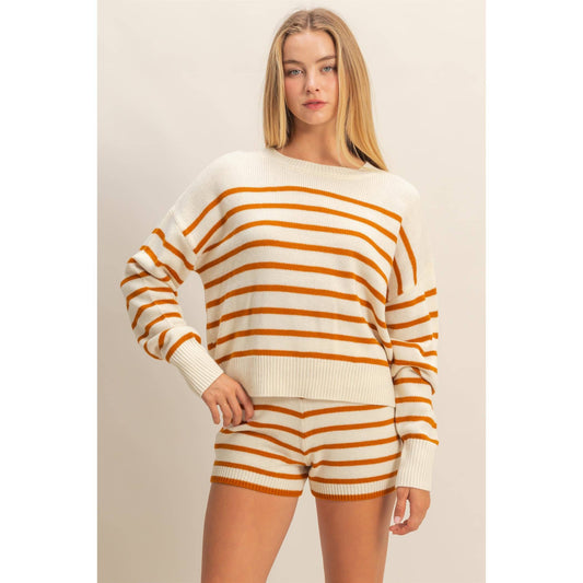 Woman wearing a white and orange striped sweater and shorts on a beige background