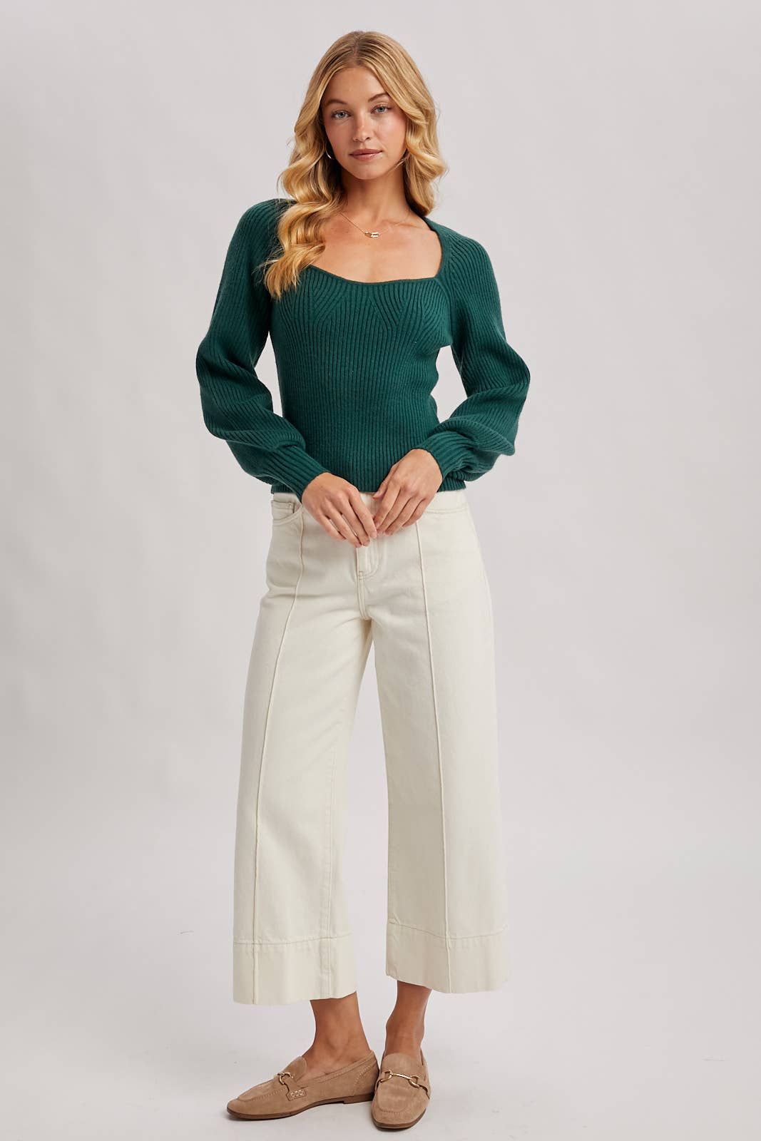 Woman wearing a green sweater and white pants on a plain background