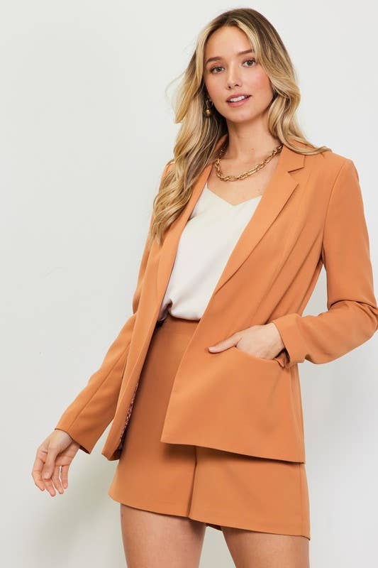 Woman wearing a brown suit with a white top on a plain background