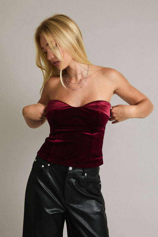 Woman wearing a burgundy velvet top and black leather pants against a plain background