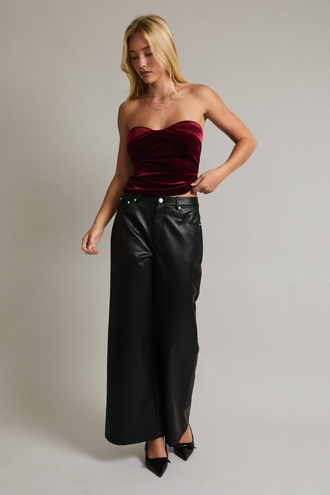 Woman wearing a strapless red velvet top and black leather pants on a plain background