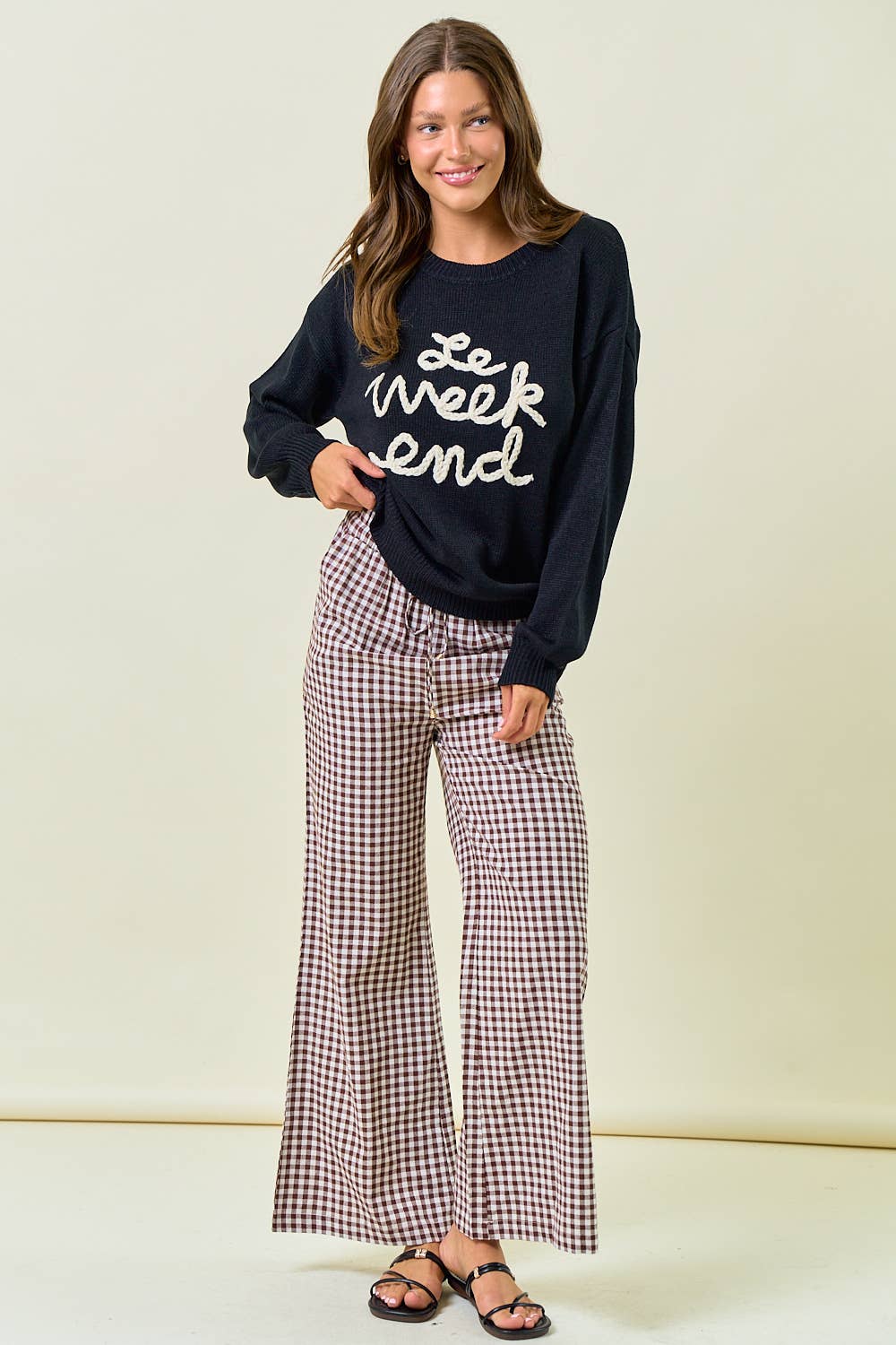 Woman wearing a navy sweatshirt with 'Le weekend' text and plaid pants on a beige background