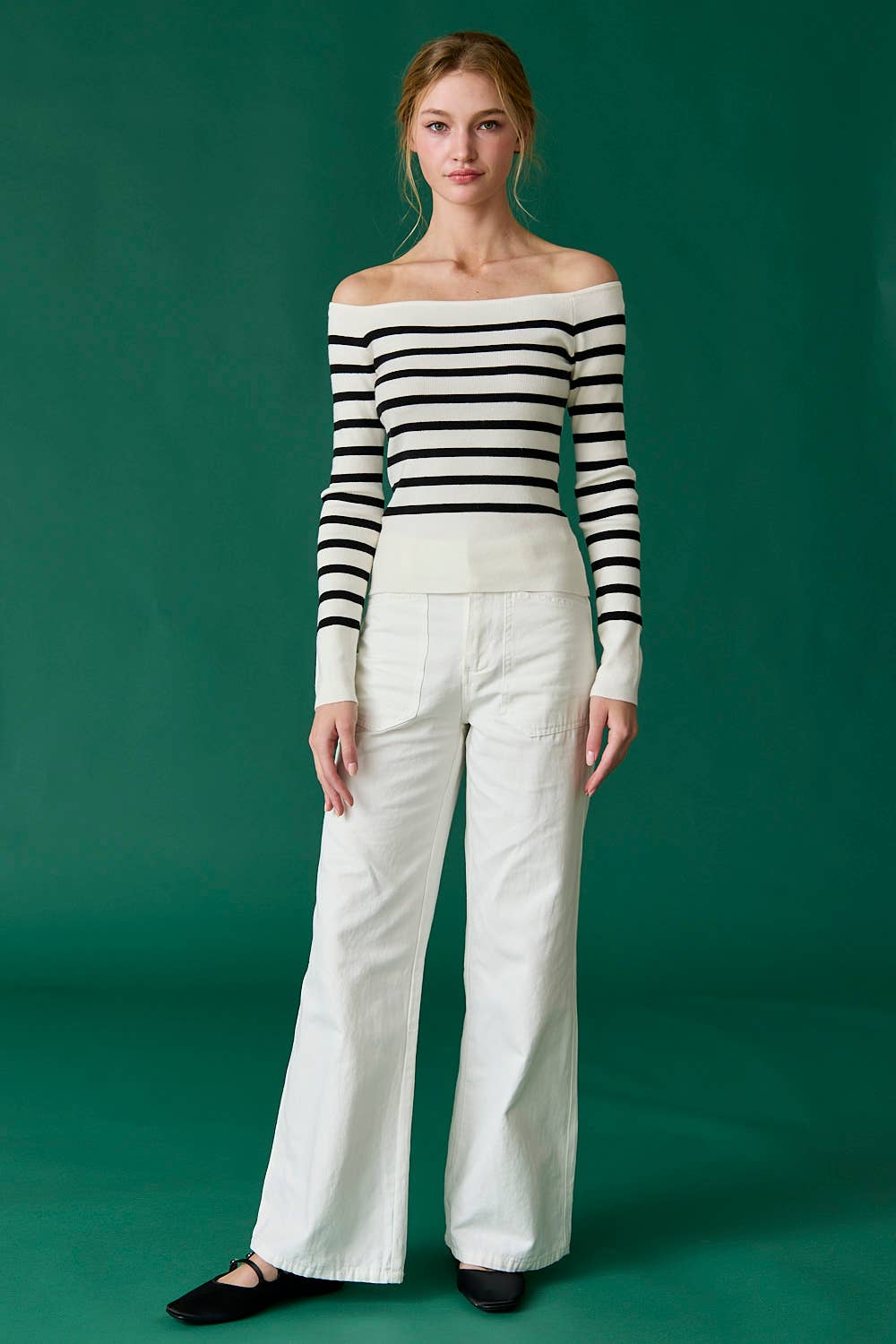 Woman wearing a black and white striped sweater and white pants against a green background