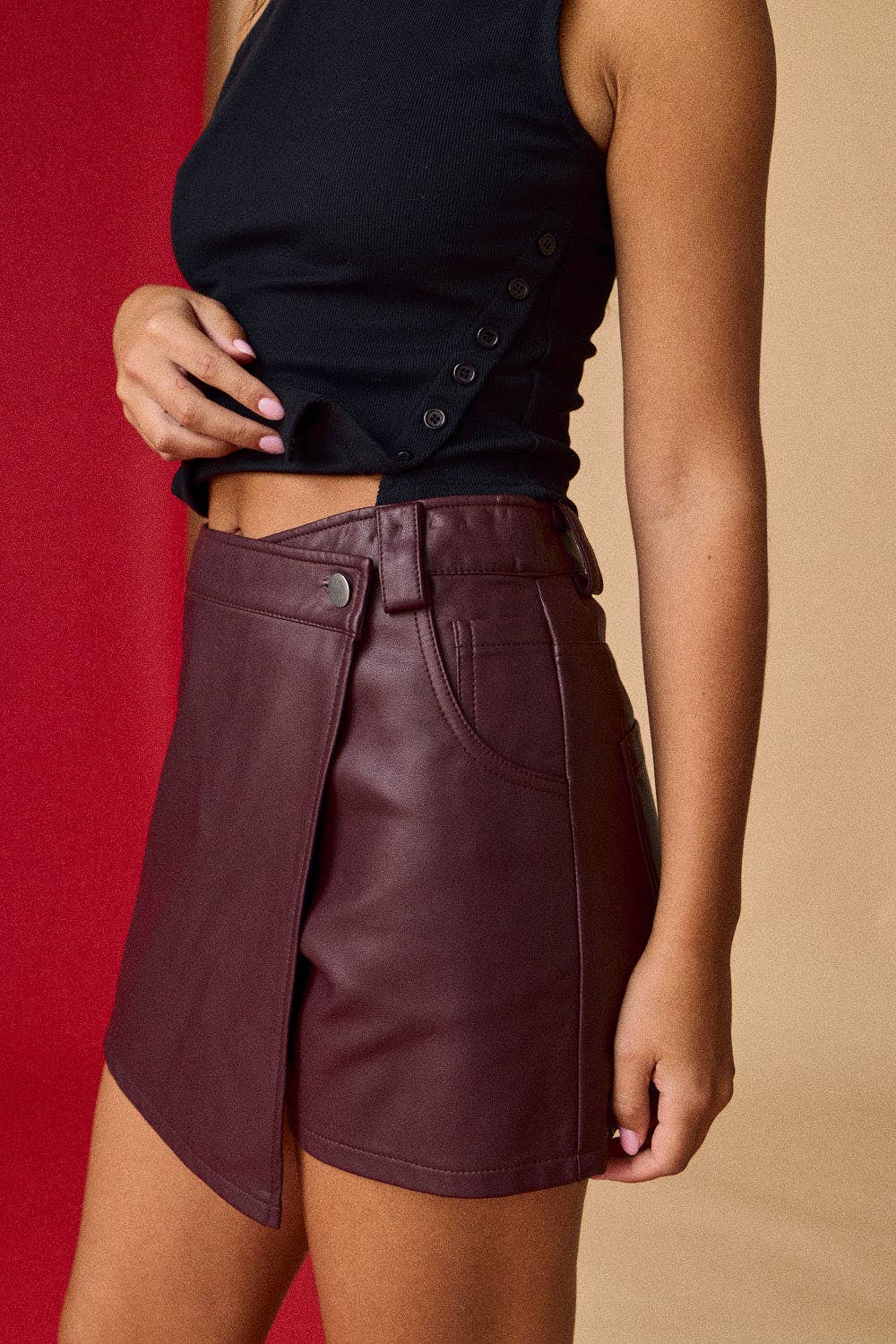 Person wearing a black top and maroon leather skirt against a red and beige background