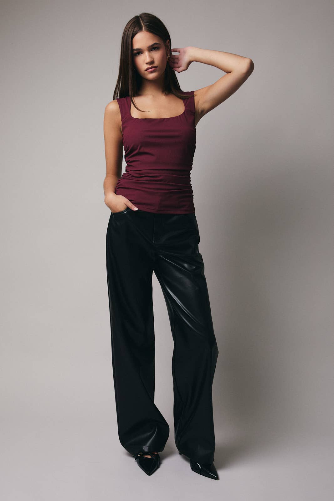 Woman wearing a burgundy top and black pants against a plain background
