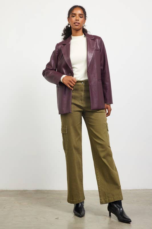 Woman wearing a purple jacket, white shirt, and green pants against a white background