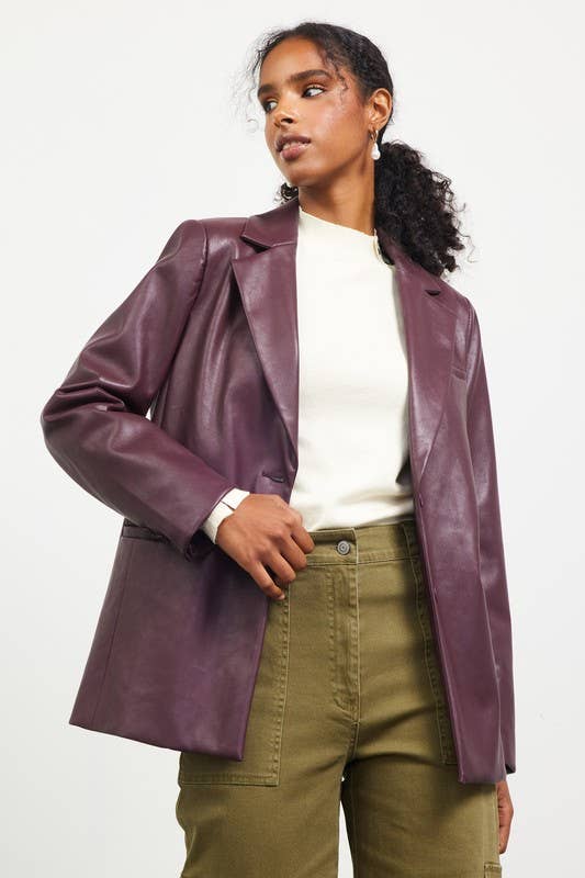Person wearing a purple leather jacket over a white shirt and green pants on a plain background