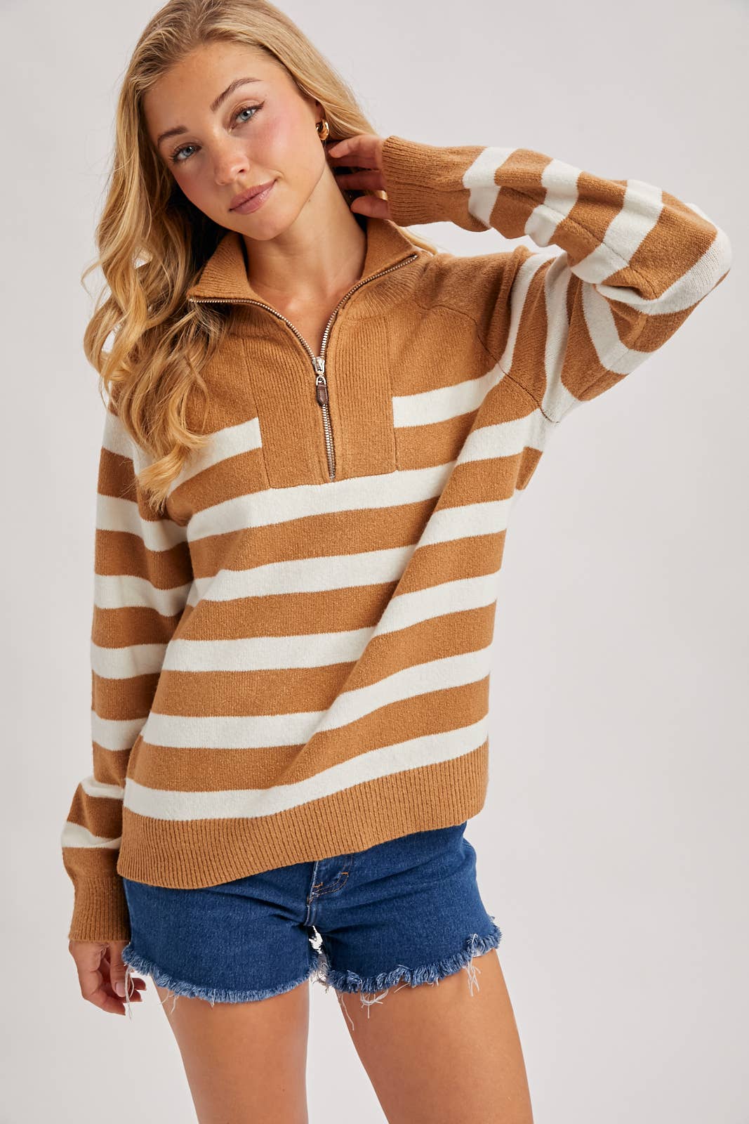 Woman wearing a brown and white striped sweater with blue shorts on a light gray background